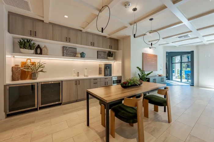 Club room kitchen area with sleek cabinetry, stylish decor, and large windows inviting natural light onto the spacious dining table.