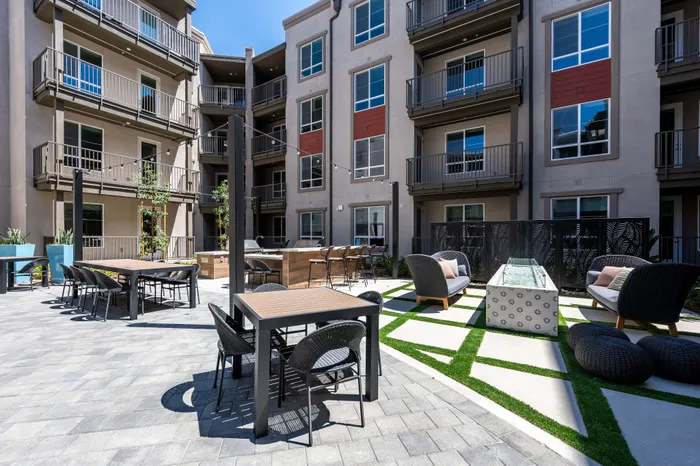 Modern apartment courtyard with stylish seating, sleek patio tables, and lush greenery, offering a vibrant outdoor social space.