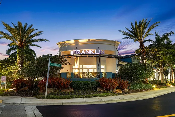 Elegant evening view of the Franklin building, surrounded by lush greenery and palm trees, with a vibrant sunset sky.