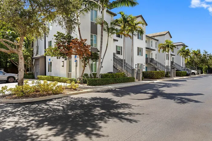Charming apartment complex with white facades and lush palm trees, featuring convenient parking and welcoming pathways.