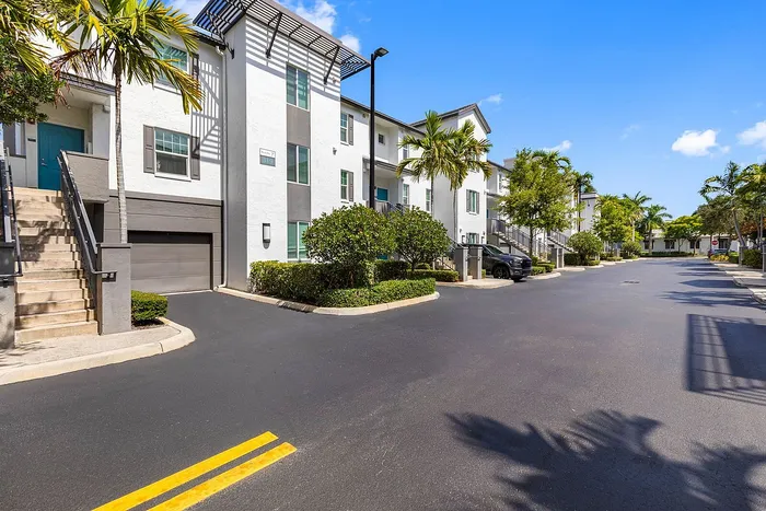 Modern apartment complex in a tropical setting, featuring white facades and palm-lined driveways under a clear blue sky.