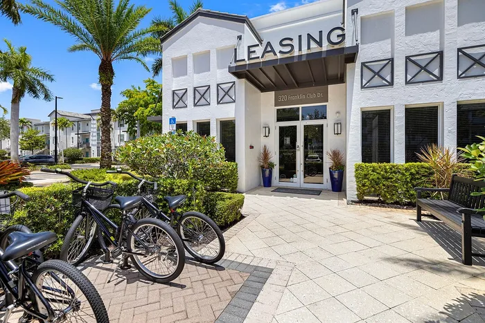 Inviting leasing office with lush greenery and bike racks in a sunny, picturesque setting.