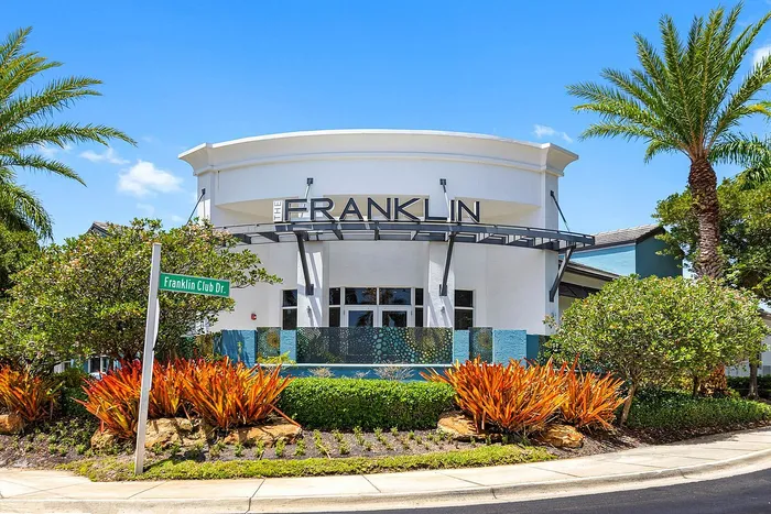 Inviting entrance to The Franklin, featuring lush landscaping and modern architecture under a bright blue sky.