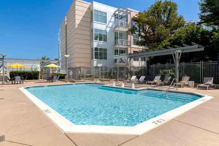 Inviting outdoor pool area with sun loungers, shaded tables, and modern apartment building in the background.