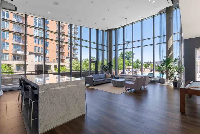 Luxurious apartment lounge with floor-to-ceiling windows, modern marble-top island, and pool views.