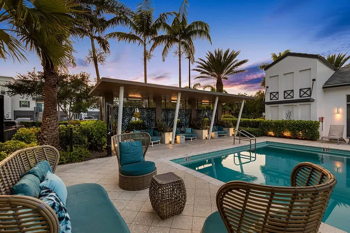 Chic outdoor lounge area with cozy seating by a sparkling pool, surrounded by lush palms, at sunset.