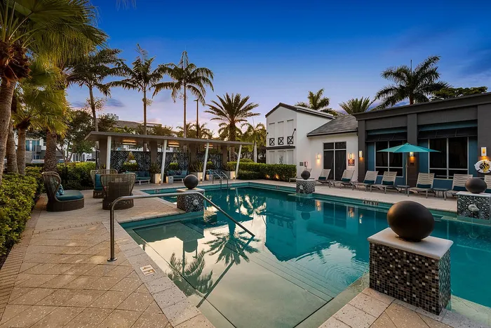 Luxurious pool area surrounded by elegant lounge chairs, modern architecture, and vibrant palm trees, perfect for relaxation and leisure.