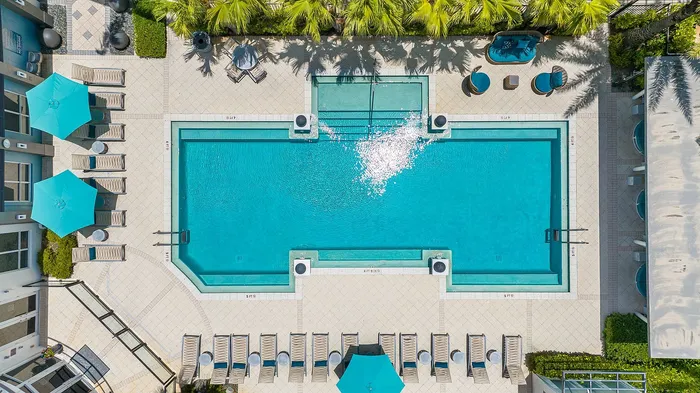 Luxurious aerial view of a sparkling outdoor pool surrounded by palm trees and stylish lounge chairs, perfect for relaxation.