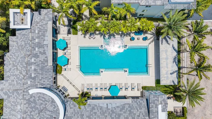 Luxurious aerial view of a modern apartment complex with a sparkling central pool, surrounded by lush palm trees and stylish lounge areas.