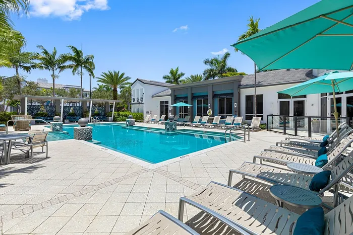 Luxurious outdoor pool area with elegant sun loungers, vibrant umbrellas, and lush palm trees, perfect for relaxation and leisure.