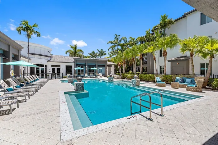 Luxurious apartment pool area with stylish lounge chairs, vibrant umbrellas, and tropical palm trees for a perfect escape.