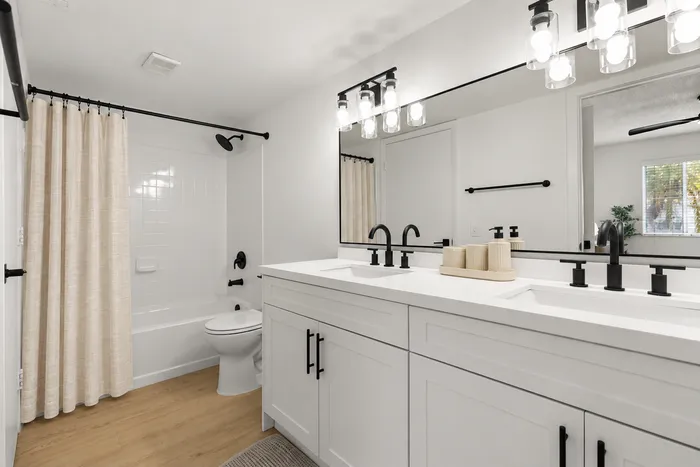 Elegant bathroom featuring a double vanity with sleek black fixtures, contemporary lighting, and a pristine white bathtub with a stylish curtain.