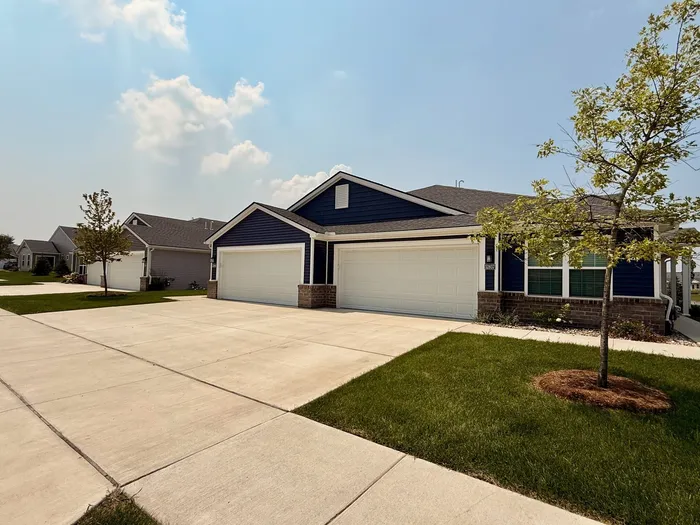 Charming suburban home with a double garage, blue siding, and manicured front lawn on a sunny day.