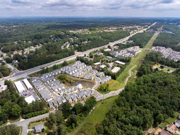Vibrant aerial view of a modern residential community, surrounded by lush greenery and easy highway access, offering a tranquil suburban lifestyle.