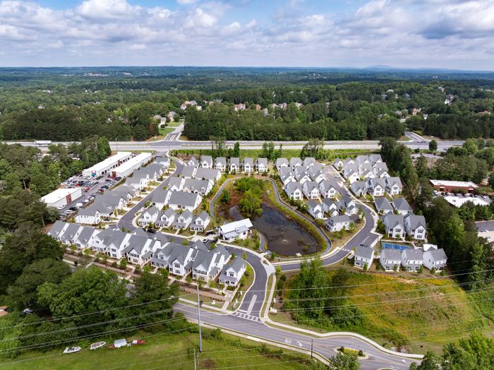 Charming aerial view of a picturesque residential community featuring elegant homes surrounded by lush greenery and a serene pond.