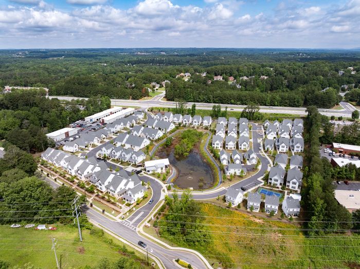 Stunning aerial view of a modern residential community with charming houses, lush greenery, and a central pond, showcasing serene suburban living.