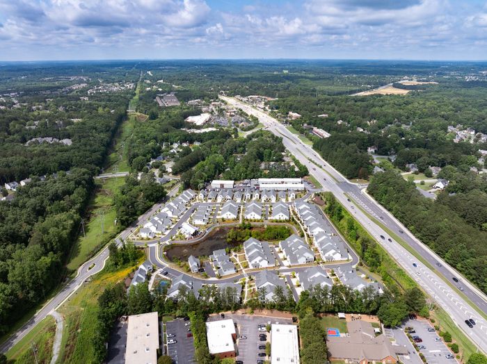 Breathtaking aerial view of a vibrant residential community surrounded by lush greenery and open roads, showcasing modern homes and serene landscapes.