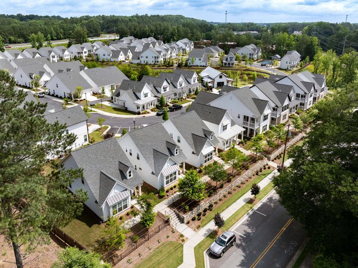 Charming aerial view of a scenic neighborhood with modern white houses, lush greenery, and well-maintained pathways, perfect for families seeking a vibrant community.