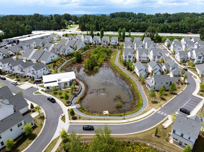 Charming suburban neighborhood aerial view showcasing cozy homes around a tranquil pond with lush greenery.
