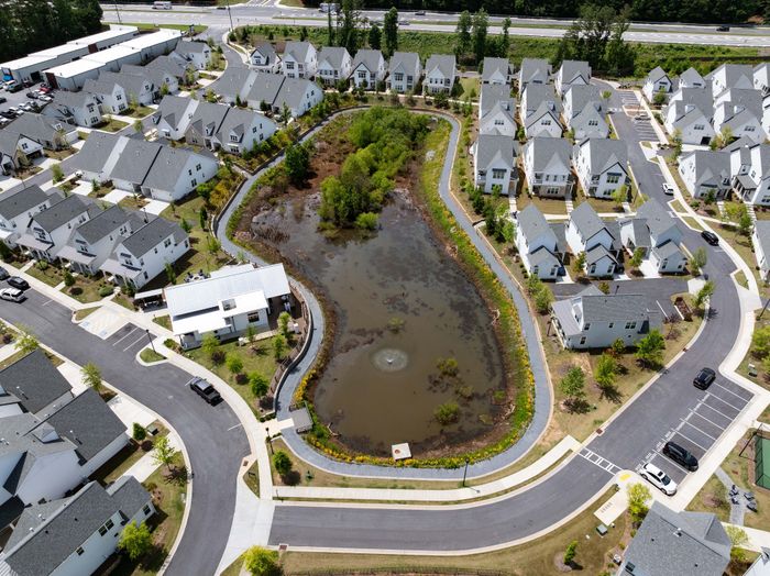 Aerial view of a charming residential neighborhood featuring modern homes surrounding a lush central pond with tree-lined pathways and well-maintained landscaping.