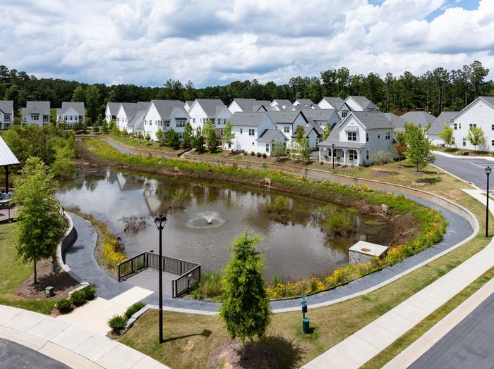 Charming suburban neighborhood with white houses overlooking a serene pond with a fountain and lush greenery.