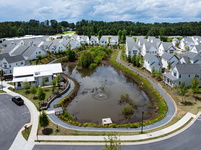 Charming neighborhood with modern white homes surrounding a serene pond and landscaped walking paths, ideal for family living.