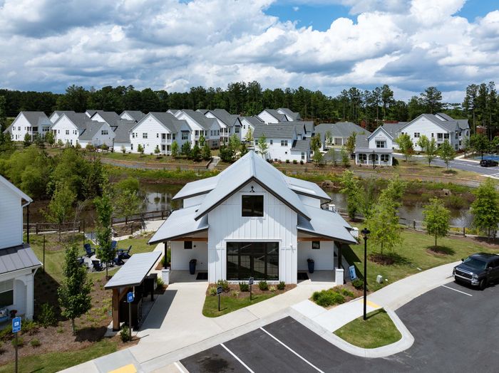 Charming suburban community with modern white-clad houses, nestled among lush greenery and peaceful water features, under a picturesque sky.