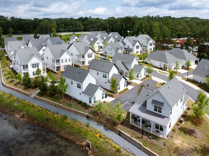 Charming suburban community with modern white houses surrounded by lush greenery and serene water features.
