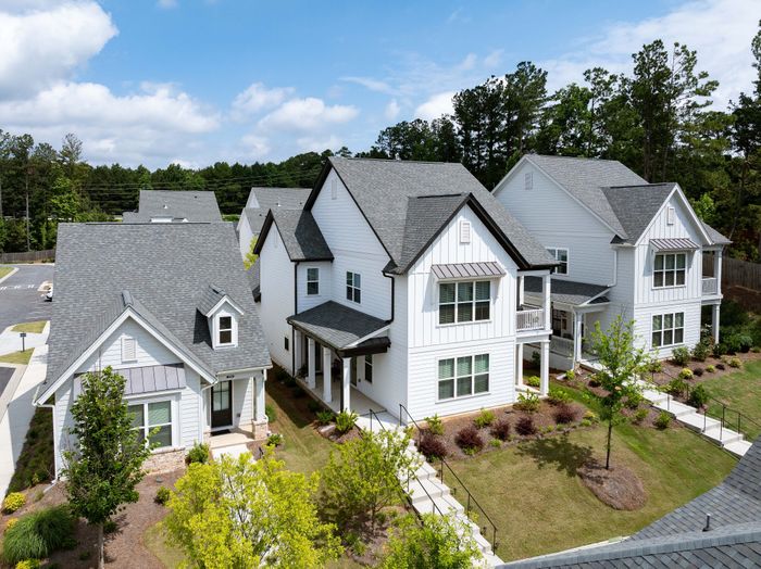 Charming suburban homes with modern architecture, featuring elegant white exteriors surrounded by lush greenery under a bright blue sky.
