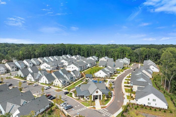 Charming aerial view of a modern suburban community surrounded by lush greenery, featuring well-designed homes and spacious streets.