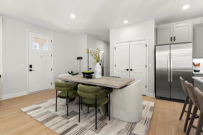 Modern kitchen and dining area with sleek stainless steel appliances, green velvet chairs, and a cozy wooden table, perfect for entertaining.