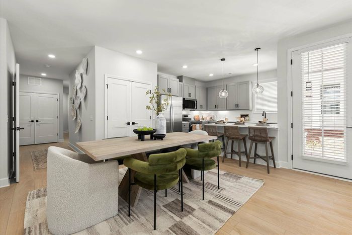 Modern open-plan kitchen and dining area with elegant gray cabinetry, stylish pendant lighting, and cozy green seating.