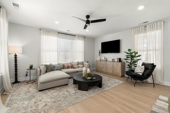 Modern living room with stylish decor, featuring a cozy sectional sofa, sleek coffee table, and wall-mounted TV against a backdrop of soft natural light and elegant curtains.