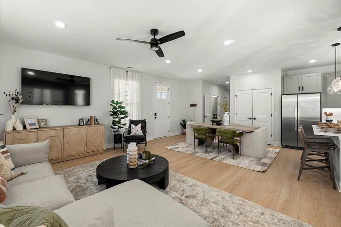 Contemporary open-plan living space featuring a cozy seating area, stylish dining table with green chairs, and modern kitchen with stainless steel appliances.