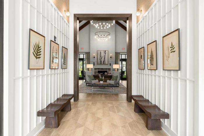 Elegant hallway with botanical artwork and sleek wooden benches leading into a luxurious living area with modern lighting.