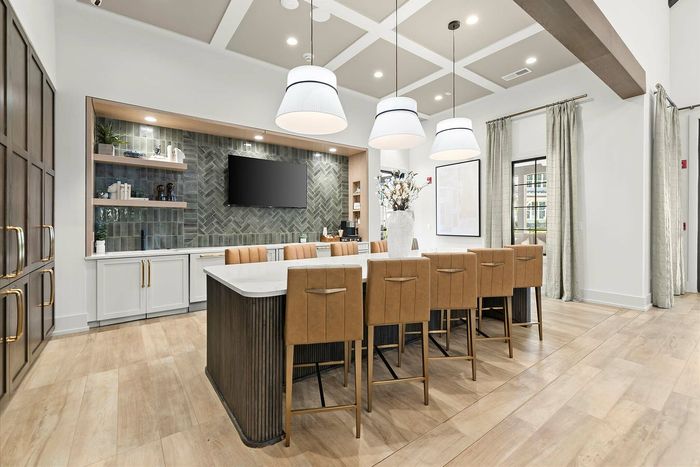 Elegant communal dining space with modern lighting, stylish bar stools, and a sleek kitchen setup featuring a prominent backsplash and built-in shelving.