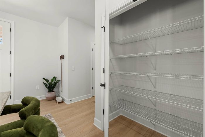 Sleek apartment corner featuring modern wire shelving, lush green armchairs, and a stylish potted plant for a touch of nature.