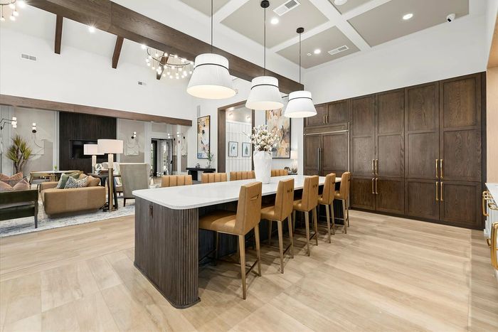Luxurious open-concept living area featuring high ceilings, elegant chandeliers, and a stylish dining island with leather seating, perfect for entertaining.