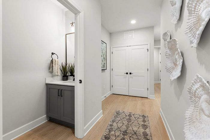 Modern hallway with elegant decor, featuring a compact bathroom with a sleek vanity, artistic wall accents, and light wood flooring.
