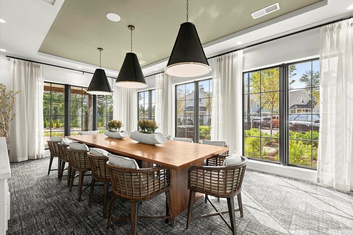 Elegant dining room with a long wooden table, stylish wicker chairs, and large windows providing abundant natural light and a lush garden view.