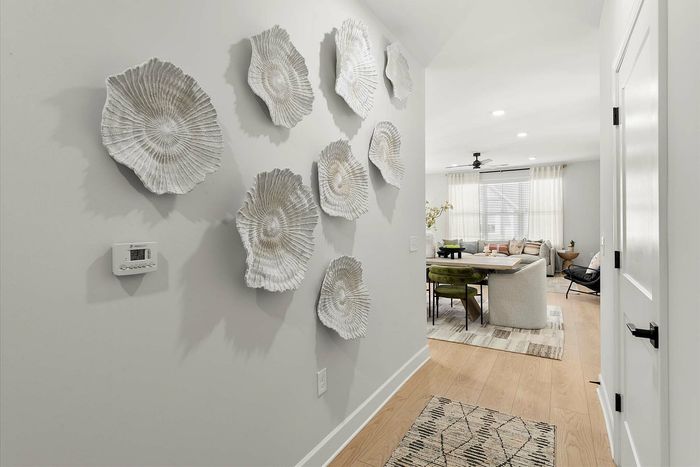 Inviting hallway with elegant wall art leading to a bright and cozy living room with modern furniture and natural lighting.