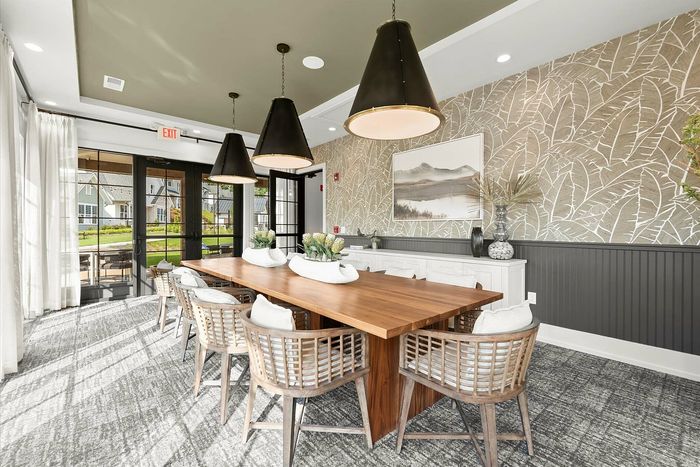 Elegant dining room with a long wooden table, stylish wicker chairs, and large pendant lights, featuring a textured wallpaper and scenic artwork, perfect for entertaining.