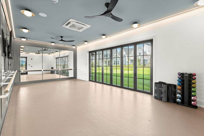 Spacious fitness studio with mirrored walls, ceiling fans, and a wall of windows overlooking lush green lawns, perfect for dance or yoga.