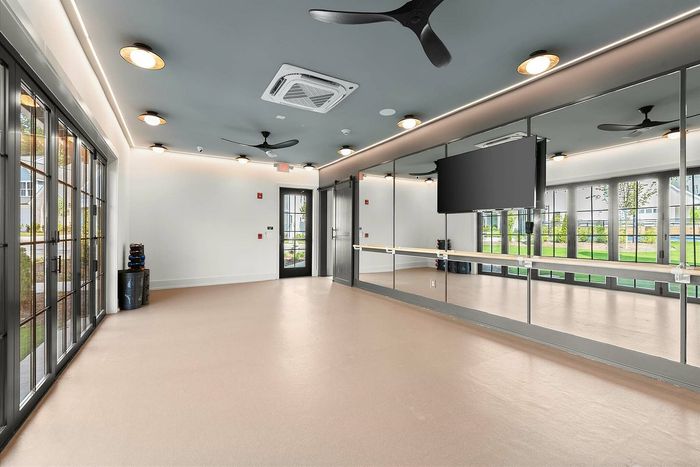 Chic fitness studio with mirrored walls, large windows, and modern ceiling fans, perfect for yoga or exercise.