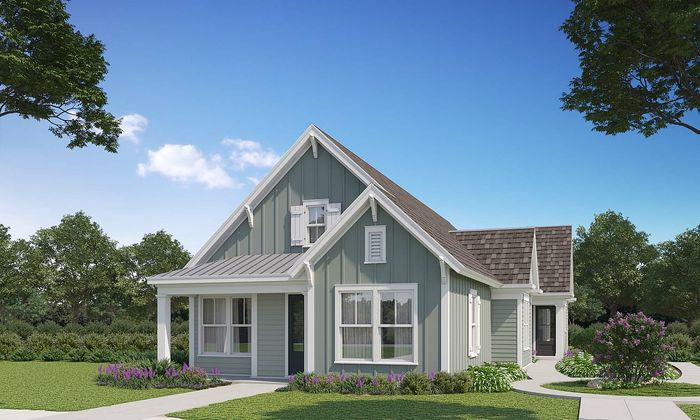 Charming single-story home with a gable roof, surrounded by lush greenery and vibrant flower beds, under a clear blue sky.