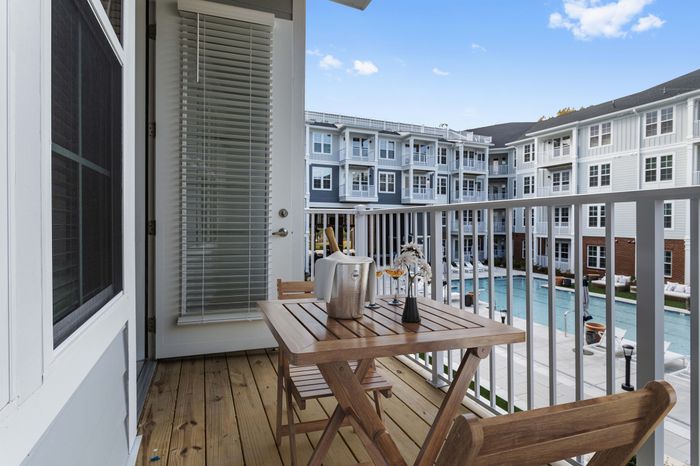 Charming balcony with wooden table set overlooking a luxurious swimming pool in a modern apartment complex.