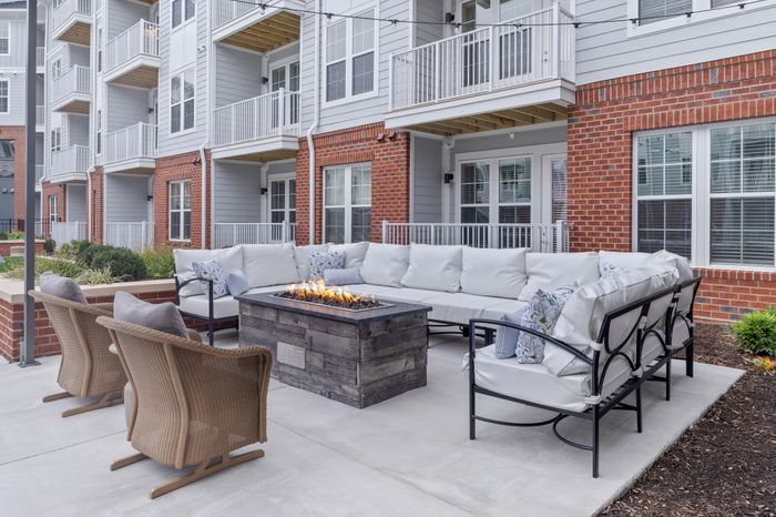 Modern apartment complex exterior with a cozy patio featuring elegant outdoor seating, a stylish fire pit, and vibrant brick facade.