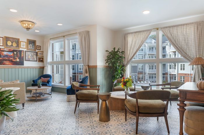 Bright and inviting living area with elegant decor, featuring cozy seating, stylish artwork, and large windows showcasing a pleasant view of the complex.