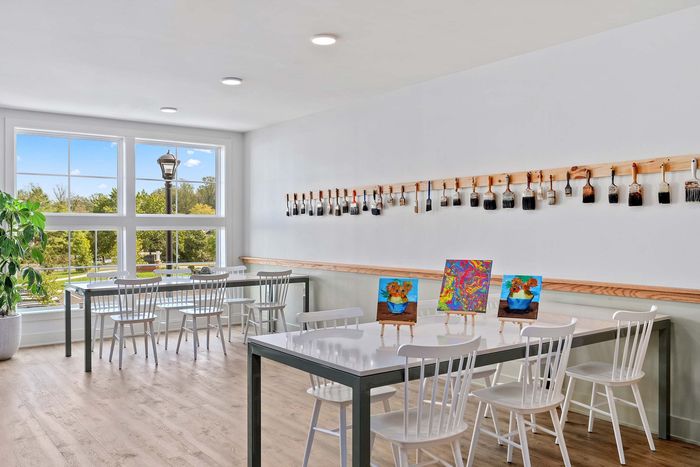 Bright and inviting art studio with large windows, white chairs, and tables displaying colorful paintings; perfect creative space with scenic views.
