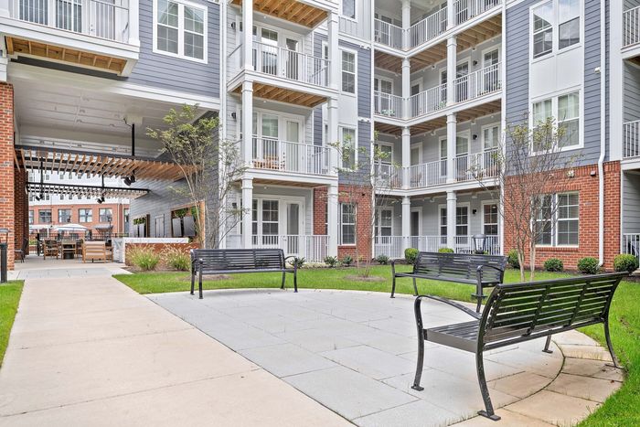 Modern apartment complex with elegant balconies overlooking a beautifully landscaped courtyard featuring cozy benches and a stylish outdoor seating area.